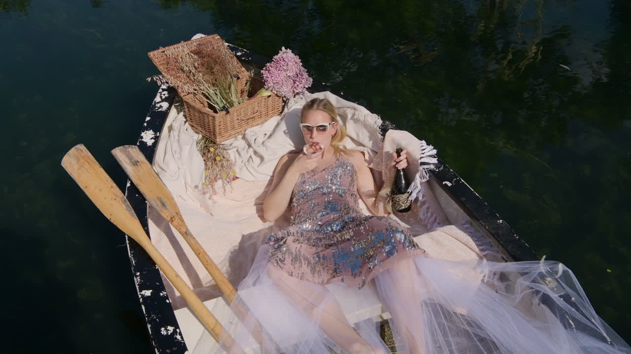 Rich girl enjoying a glass of expensive champagne in rowboat floating in lake