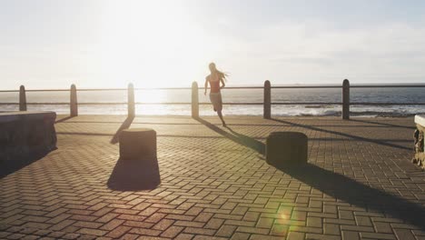 african american woman running on promenade by the sea at sundown