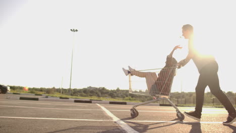 Young-friends-having-fun-on-shopping-trolleys.-Multiethnic-young-people-racing-on-shopping-cart.-slow-motion