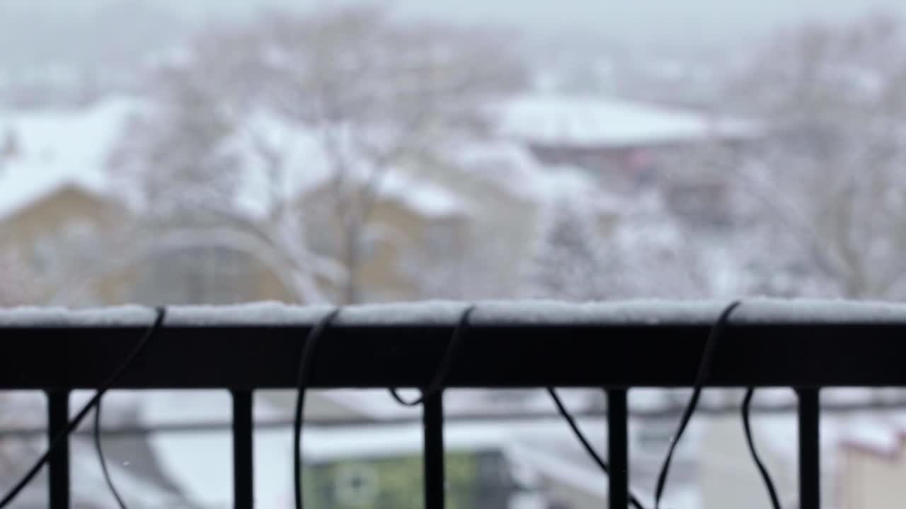 슬로우 모션 샷은 12월 유타 미드베일에 있는 아파트 발코니 난간과 기타 건물 및 나무가 배경에 초점이 맞지 않는 오래된 겨울 눈보라 동안 떨어지는 눈송이를 닫습니다.