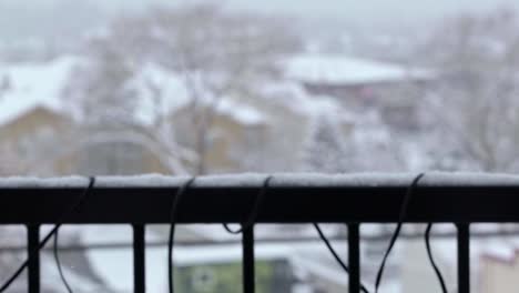 disparo en cámara lenta cerca de copos de nieve cayendo durante una vieja tormenta de nieve invernal con una barandilla del balcón de un apartamento y otros edificios y árboles desenfocados en el fondo en midvale utah en diciembre