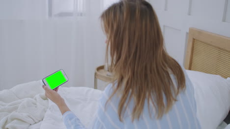 hermosa mujer usando pantalla táctil de teléfono inteligente en una habitación luminosa. joven mujer morena atractiva habla a través de una videollamada en la cámara web del teléfono inteligente con un amigo en el dormitorio por la mañana
