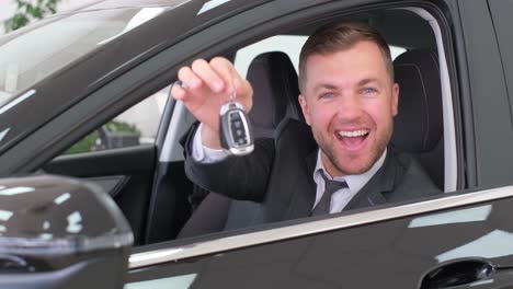 young european driver in car, sharing concept, vehicle and premium transport. happy guy driving, sitting in a new luxury car, showing the keys