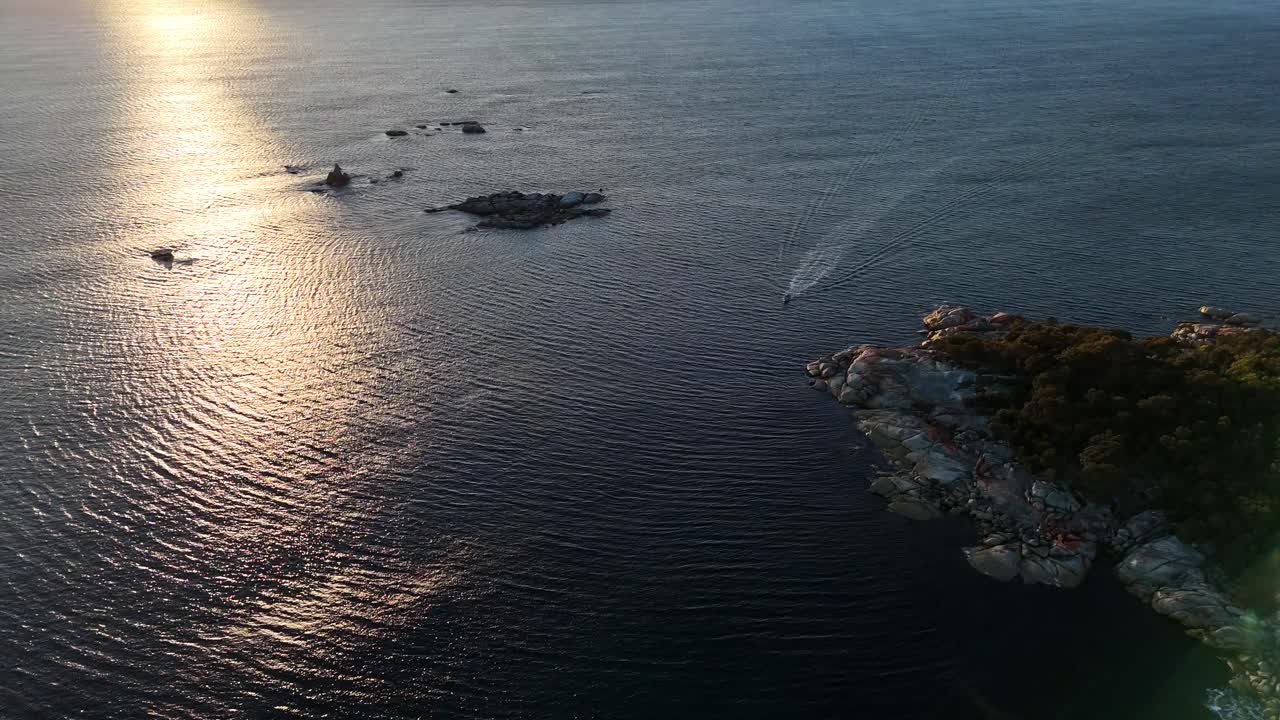 Aerial View of a Boat on the Ocean near a Rocky Coastline at Sunset