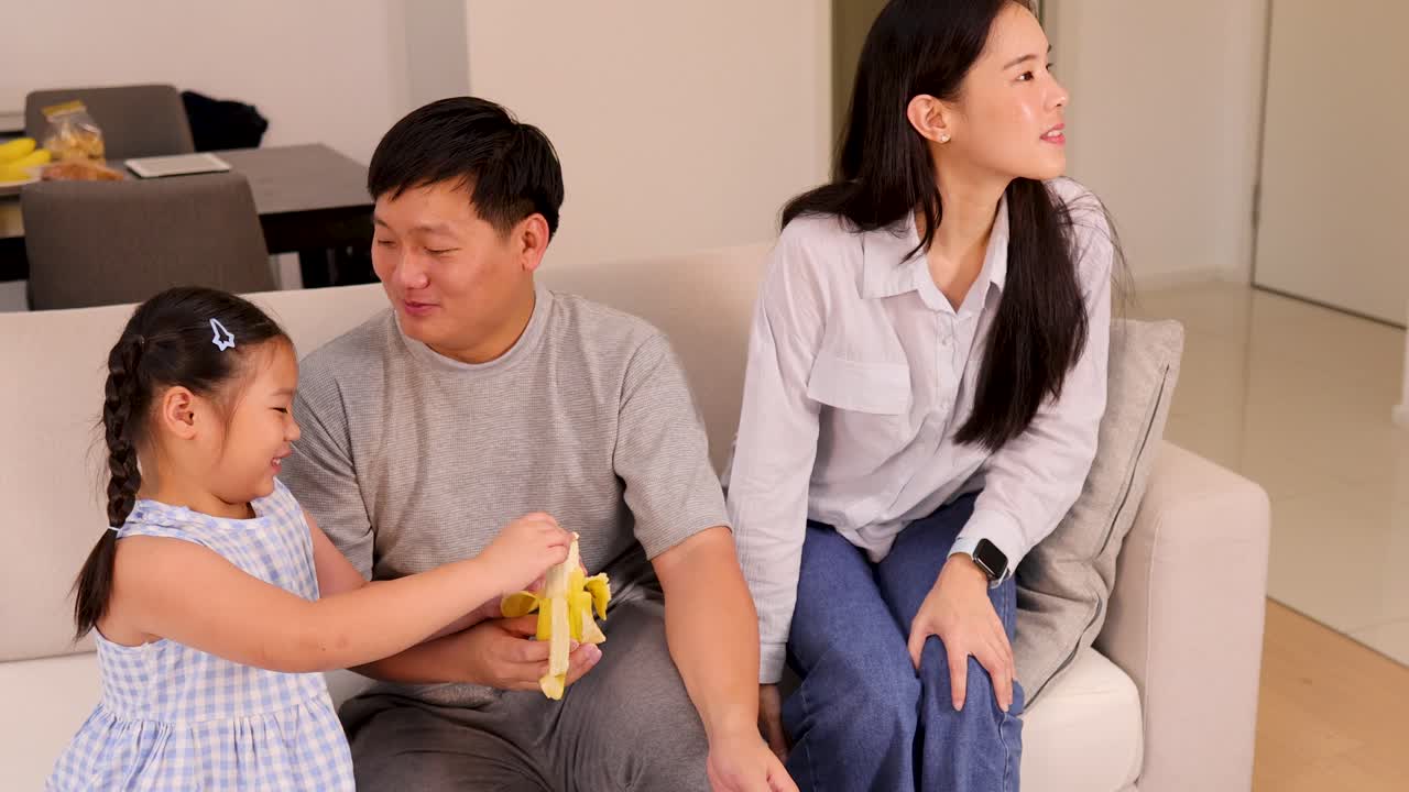 A family enjoys a casual moment together on a sofa, sharing snacks and conversation in a bright, cozy living room