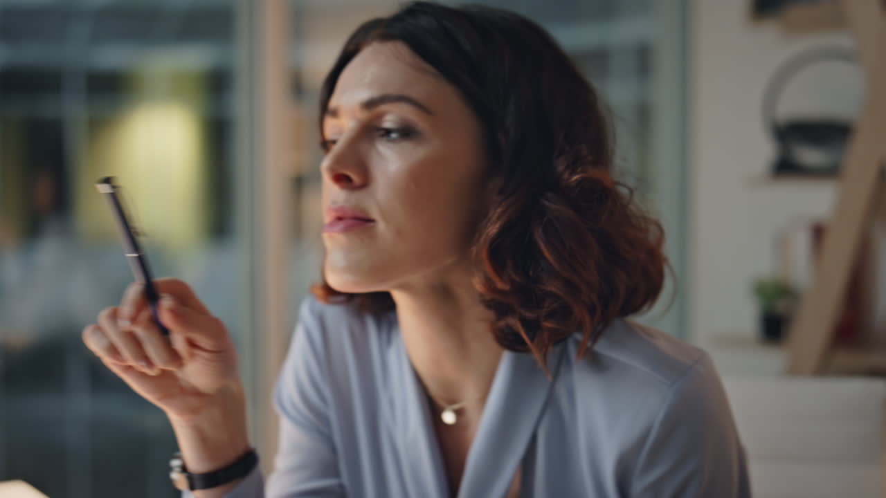 Thoughtful woman holding pen pondering ideas at evening workplace closeup