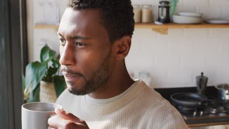 Happy-african-american-man-standing-in-kitchen,-drinking-coffee