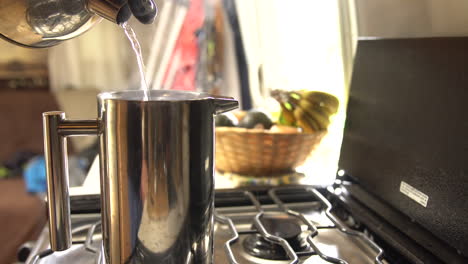 man pours boiling water from a tea pot into a stainless steel french press