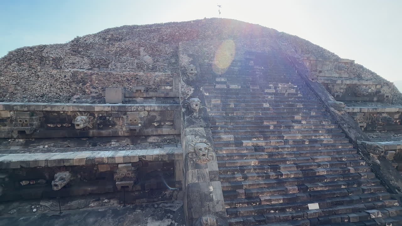 Vista illuminata dal sole della scalinata del Tempio di Quetzalcoatl a Teotihuacan con dettagli in pietra scolpita e bagliore dell'obiettivo, che mostra l'antica architettura messicana e le rovine storiche.