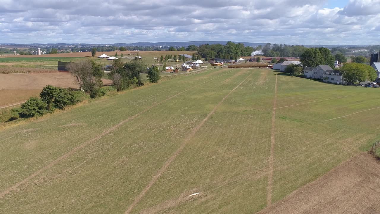 vista aérea del campo agrícola con un tren de vapor antiguo acercándose a través de él en un día soleado parcialmente nublado visto por un dron