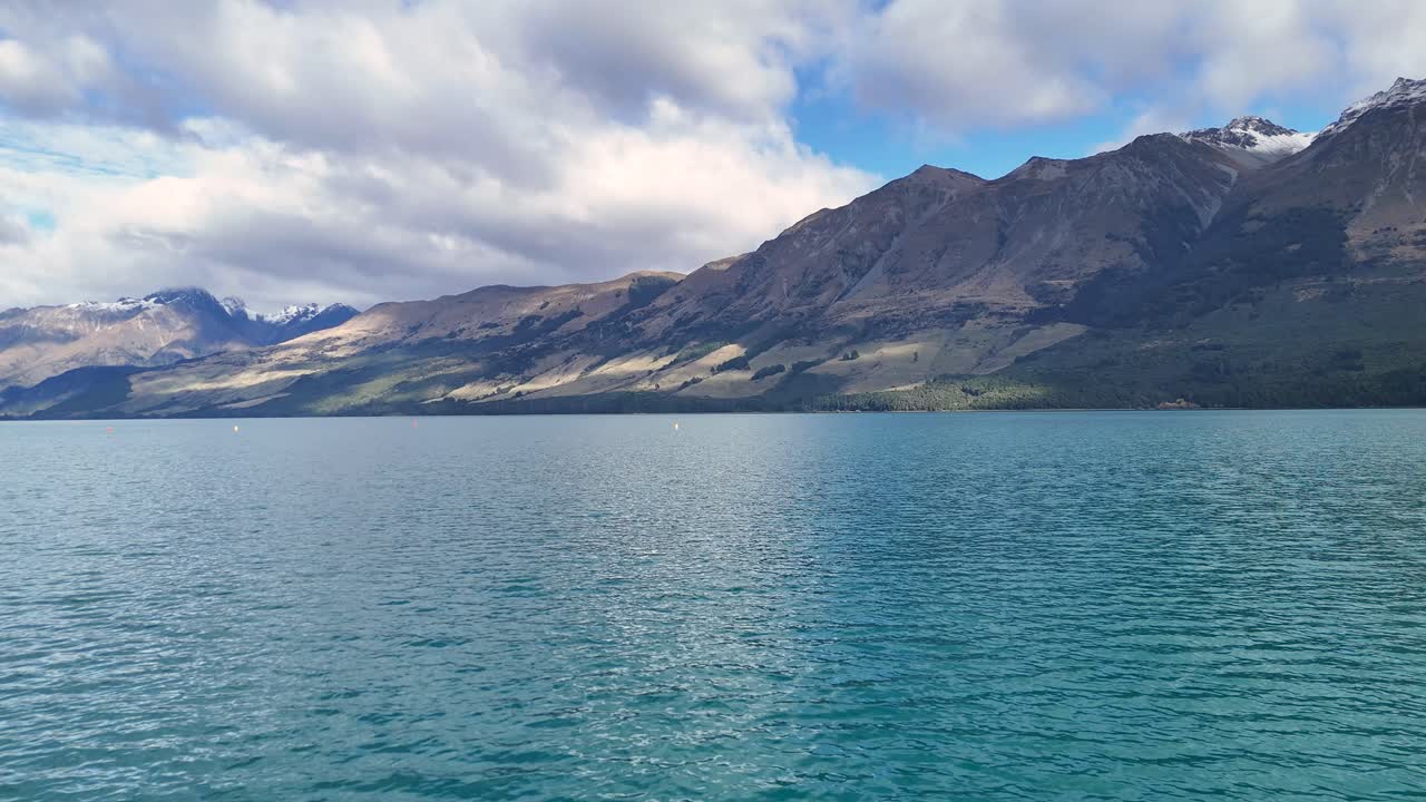 Tranquil lake with majestic mountains under a partly cloudy sky. Calm waters reflect the natural beauty of Glenorchy, New Zealand
