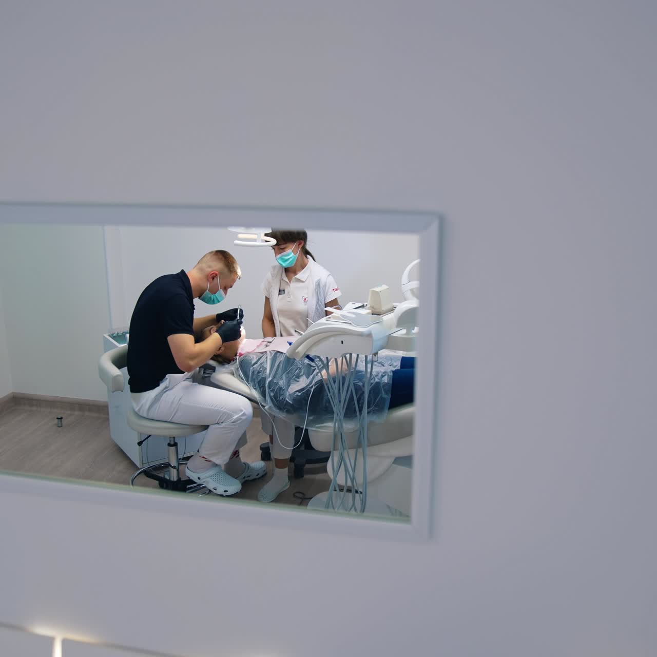 Treatment of teeth in dental office. Stomatologist man and female assistant working in a modern dental cabinet. Dental health. View from the small window on dental procedure