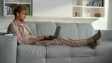 man working home office in pajamas. focused ginger student using laptop computer