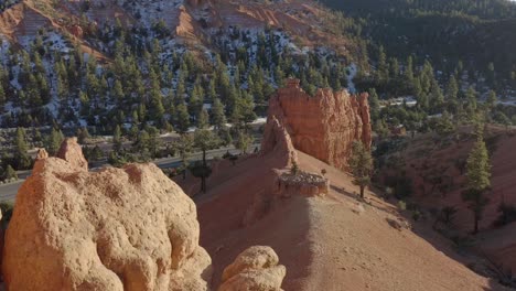a drone shot of the sandstone rocks of red canyon area near bryce canyon in the winter and a van is seen driving on the below