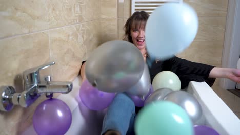 Young-Woman-Sitting-at-Bathtub-Throwing-Balloons-at-Bathroom