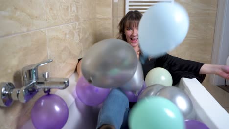 mujer joven sentada en la bañera tirando globos en el baño