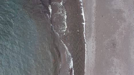 aerial-drone-view-looking-down-on-grey-beach-with-waves-of-lake-superior-lapping-on-shoreline-getting-closer-descending-zooming-down-toward-sand-in-day-light