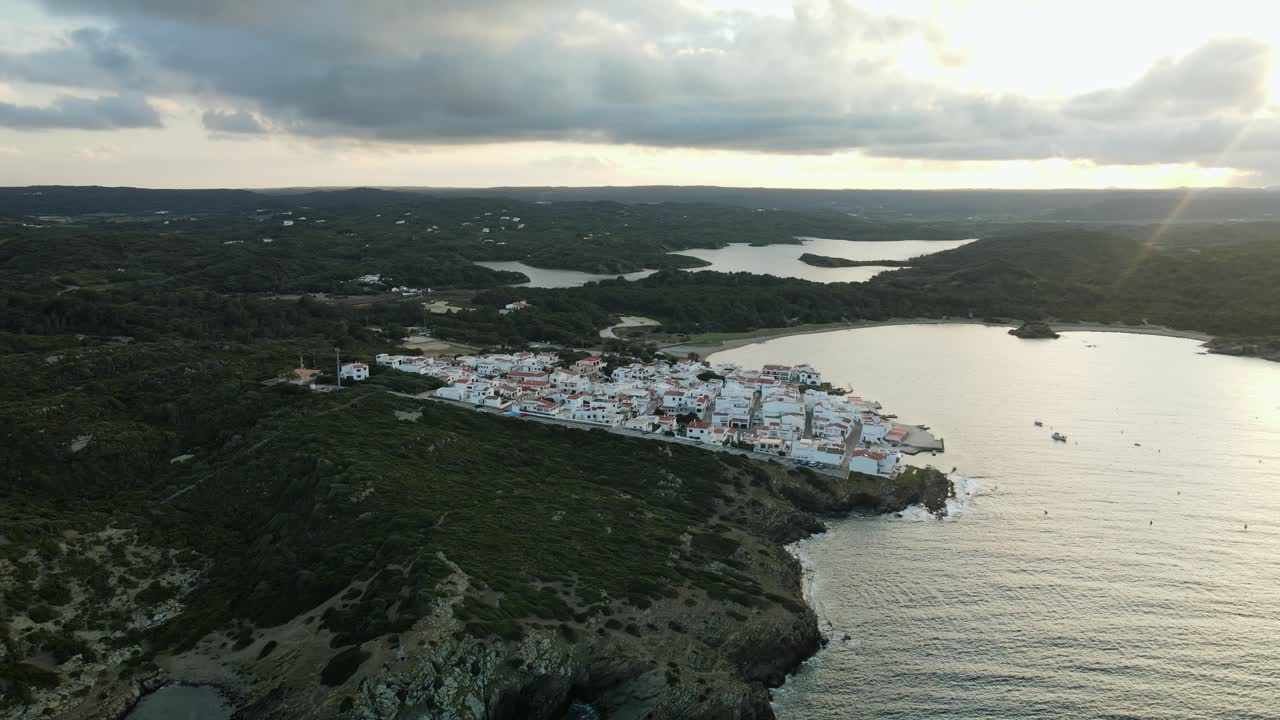 Small village along the hills of Es Grau in Menorca with sun setting behind the clouds
