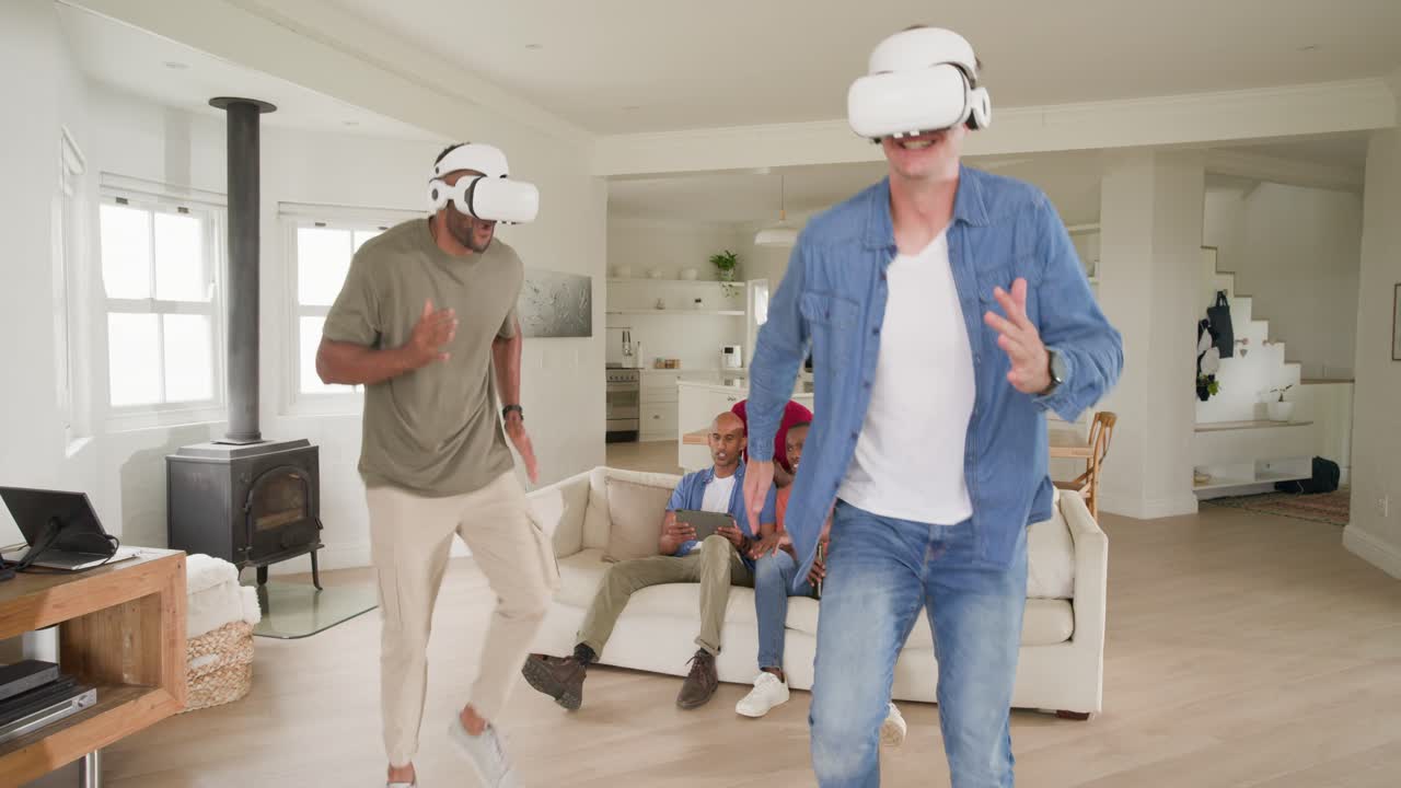 Video verticale: Uomini di diverse etnie che osservano due uomini indossare visori VR e giocare a un gioco VR a casa.