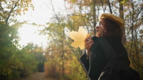 lady walking through forest path adjusting bag with yellow beret and sunglasses as warm sunlight creates a glowing effect around her, enhancing the autumn atmosphere and peaceful nature scenery