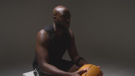 studio portrait shot of seated male basketball player with hands holding ball