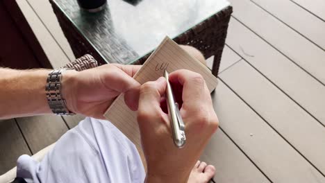a man writes a story in a small book with his pen