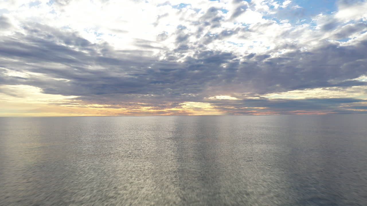 항공:해수면의 하늘에 반사되어 하늘에 주황색과 파란색이 있는 장엄한 지평선과 함께 황금시간대에 뒤로 비행