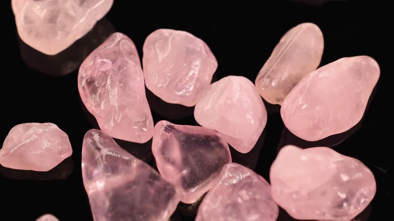 Rose quartz stones spin gracefully against a dark backdrop, highlighting their pink hues and smooth textures under soft lighting