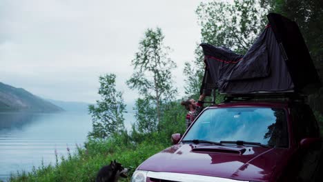 male camper setting up car roof top tent on the shore of leirfjord in sorfold, norway