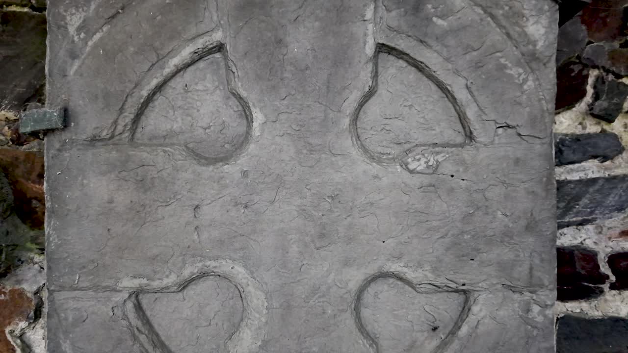 Ancient Manx cross stone tablet with carved circular motifs set against a stone wall