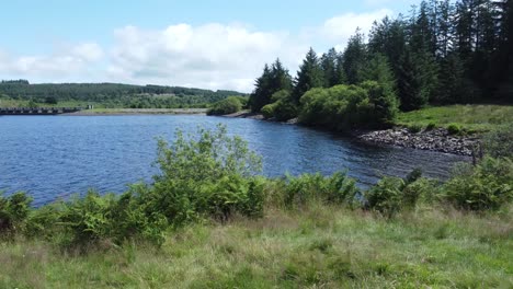 idyllic blue water reservoir lake woodland hiking walk aerial view dolly right across shore