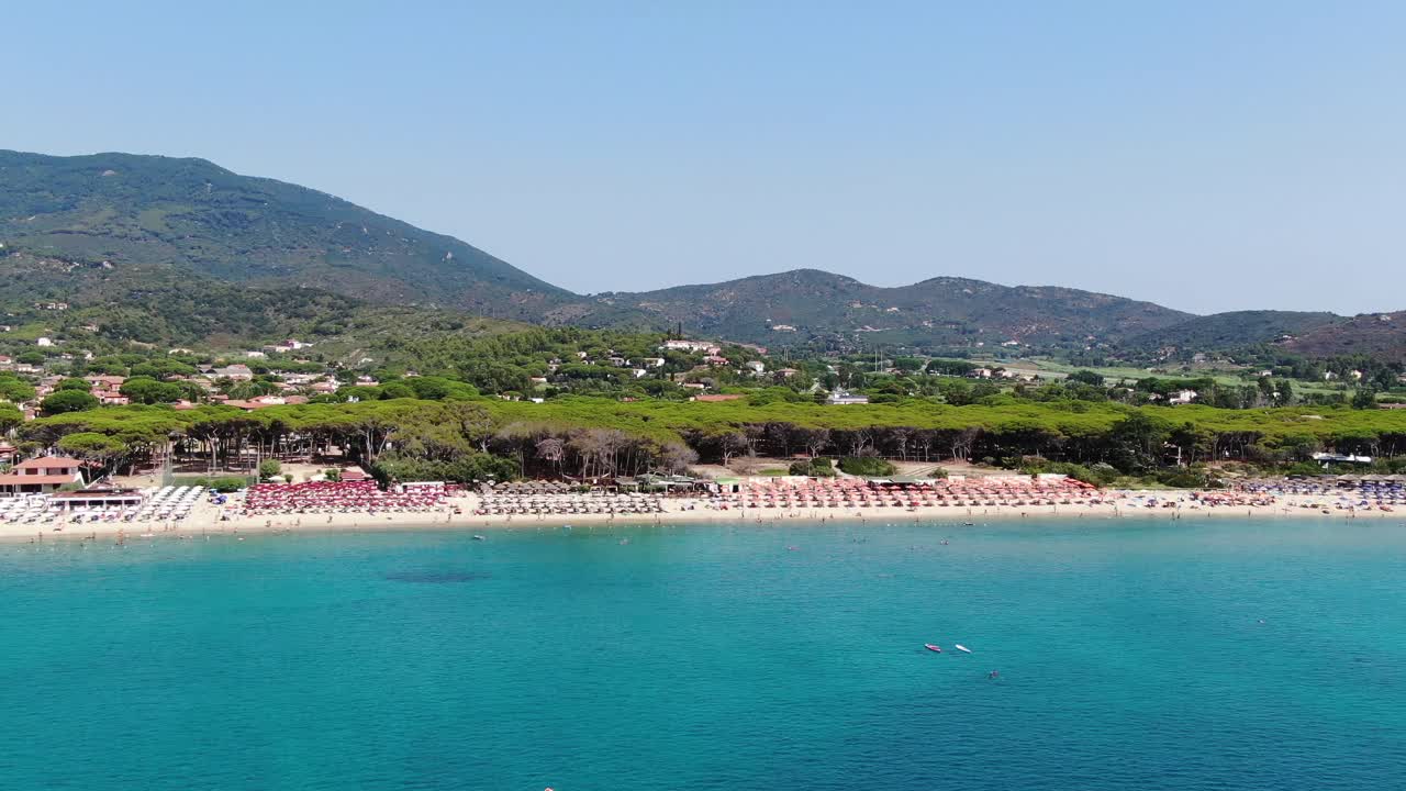 People paddling, floating, and playing in turquoise waters with colorful boats in the background