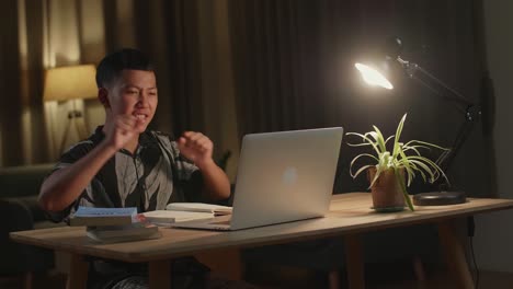 young asia boy student celebrating with laptop computer at home, teenage boy learning online from laptop at night