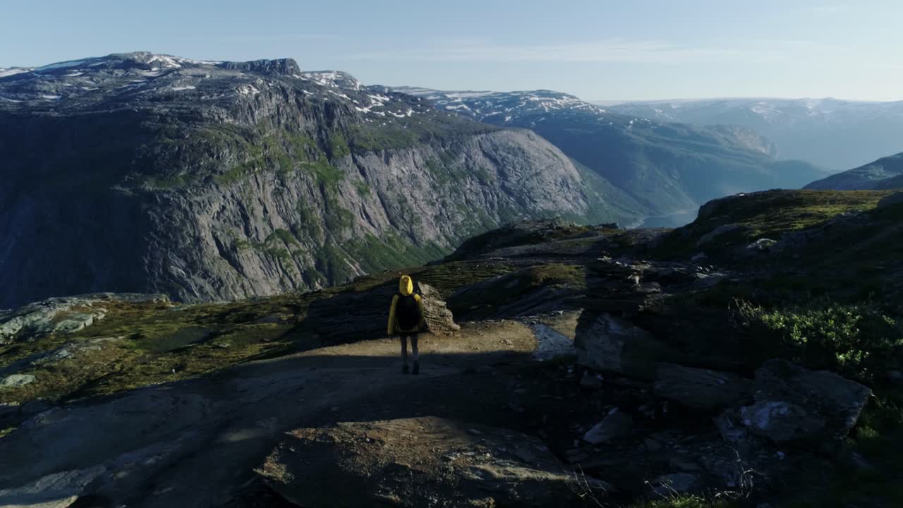 Woman in yellow jacket walking through mountain trail near Trolltunga Norway