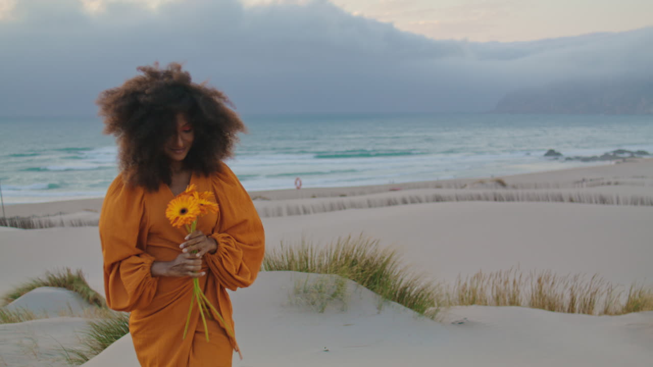 niña posando en una playa ventosa con un hermoso ramo de naranja en primer plano. mujer con flor