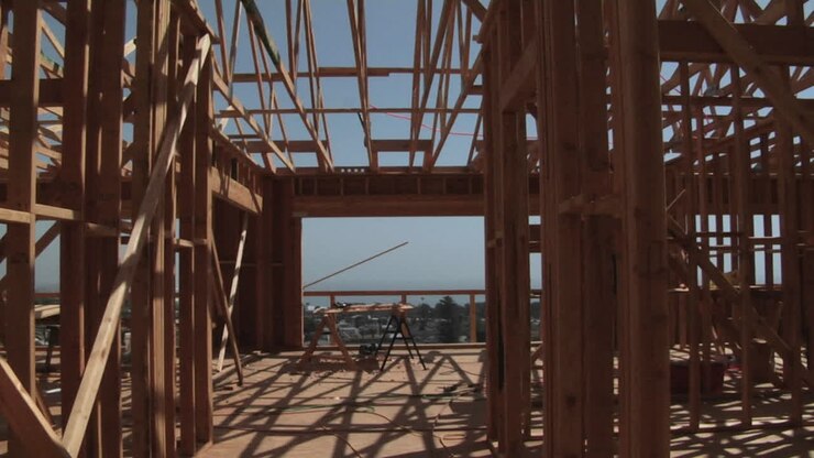 Een aannemer draagt een stuk hout in een onafgebouwd huis