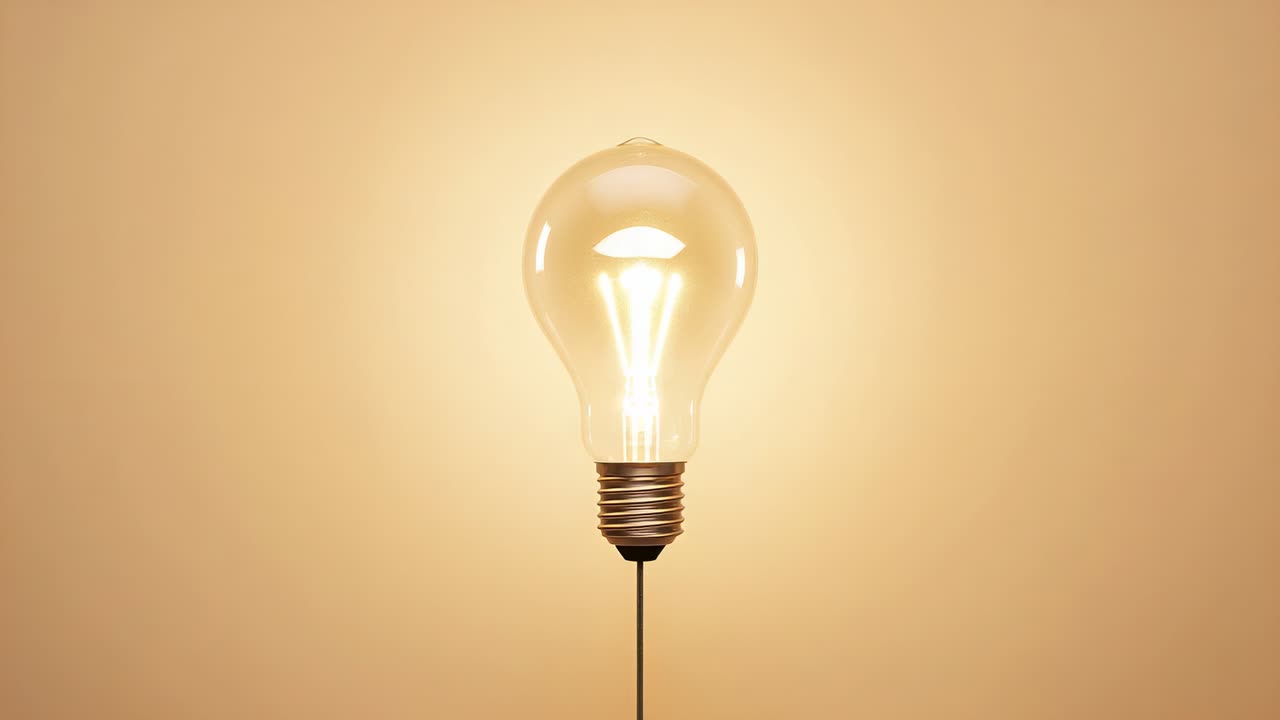 Current arriving powering incandescent bulb on cord before beige wall, filament glowing brighter