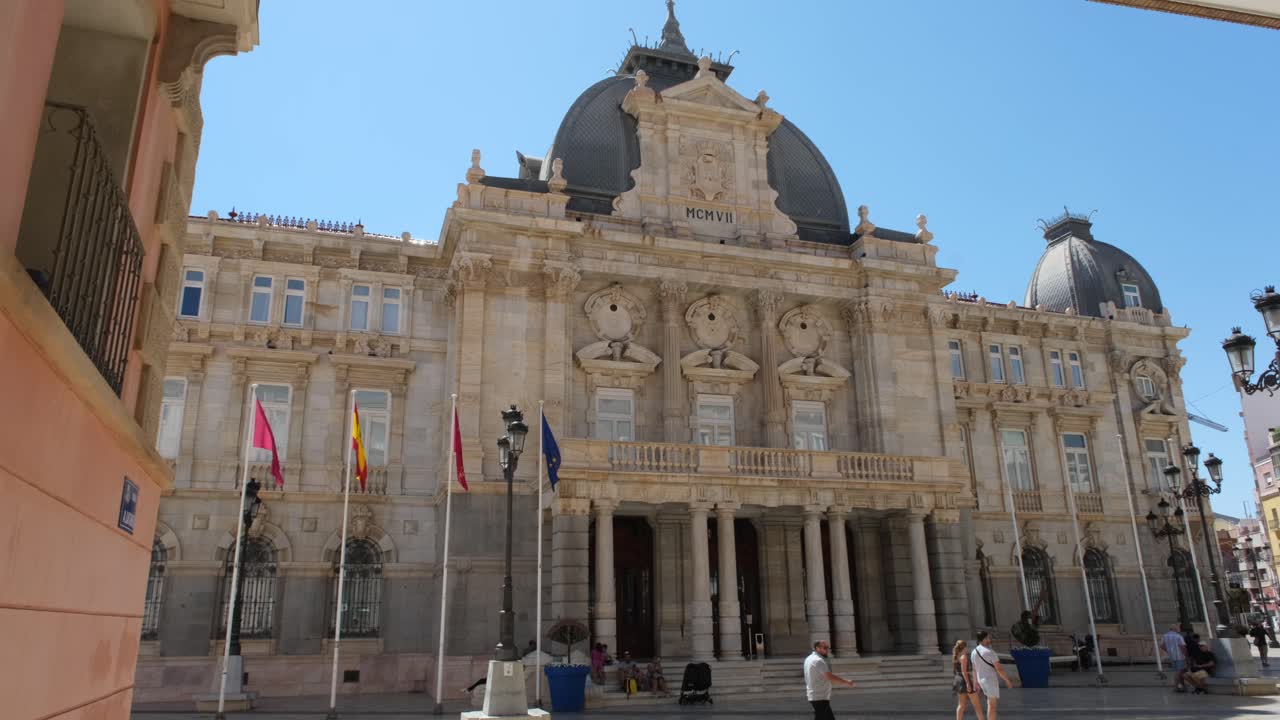 A front view of the majestic City Hall building, or Palacio Consistorial, with people walking back and forth, capturing the lively atmosphere of the area.