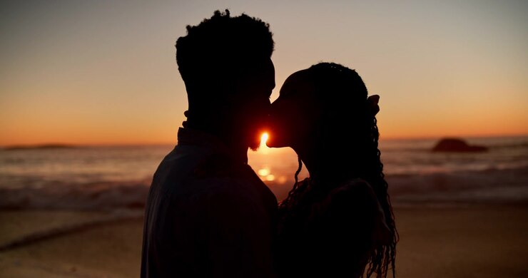 Silhouette di una giovane coppia che si bacia sulla spiaggia al tramonto