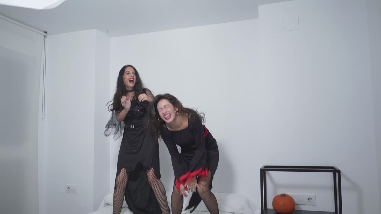 Two Women in Halloween Costumes Jumping on a Bed