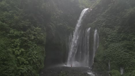 tourist man uses selfie stick camera in mist below tiu kelep waterfall