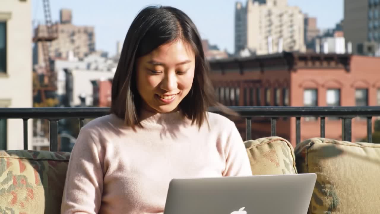 A Young Woman Enjoys a Relaxing Moment on Her Balcony, Engaged in Digital Activities with a Laptop Against a Scenic Urban Background