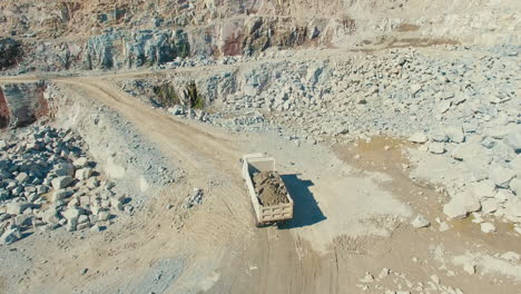 Camión-Cargado-Conduciendo-En-Cantera-Mineral-Granito-Piedra-Grava,-Amplio-Disparo-Aéreo-De-Drones