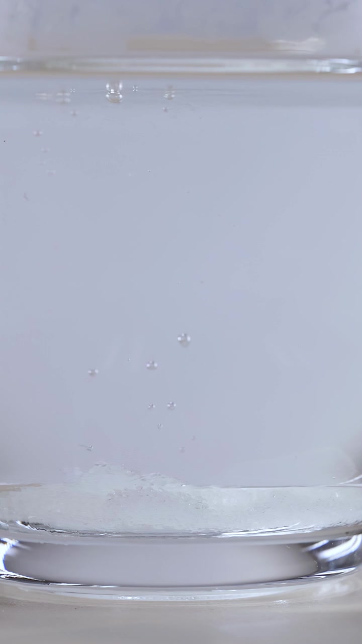 Gros plan macro d'un morceau de sucre blanc se dissolvant dans de l'eau claire avec des bulles d'air qui montent