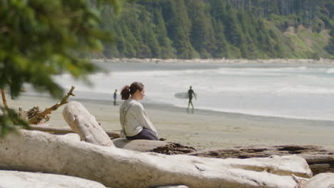 Woman-on-serene-Beach-Looking-Out-Over-the-Ocean,-Surfer-Walks-with-Surfboard