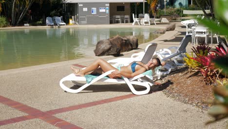 chica sexy en traje de baño de dos piezas tomando el sol en un sillón junto a la piscina