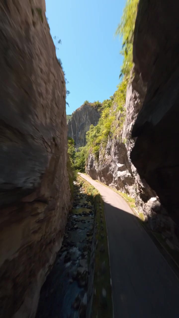 A breathtaking vertical perspective flying through a narrow limestone gorge with a mountain river and road in Asturias, Spain. Ideal for travel social media and wellness content.