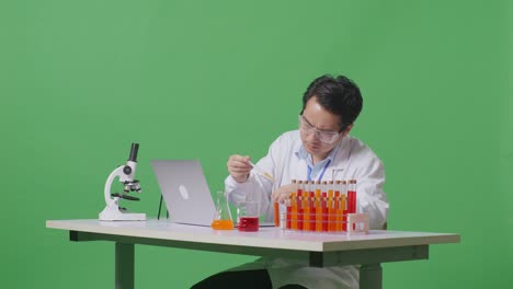 side view of asian man scientist making experiment with test tube and saying wow while working on a laptop on the table with microscope in the green screen background laboratory