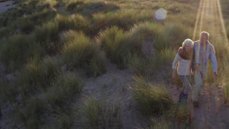 drone shot of senior couple walking across dunes on winter beach vacation