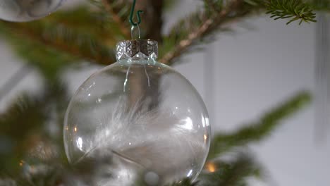 Extreme-close-up,-white-feather-inside-transparent-Christmas-bauble,-elegant-homemade-X-mas-ornament,-tilting-up